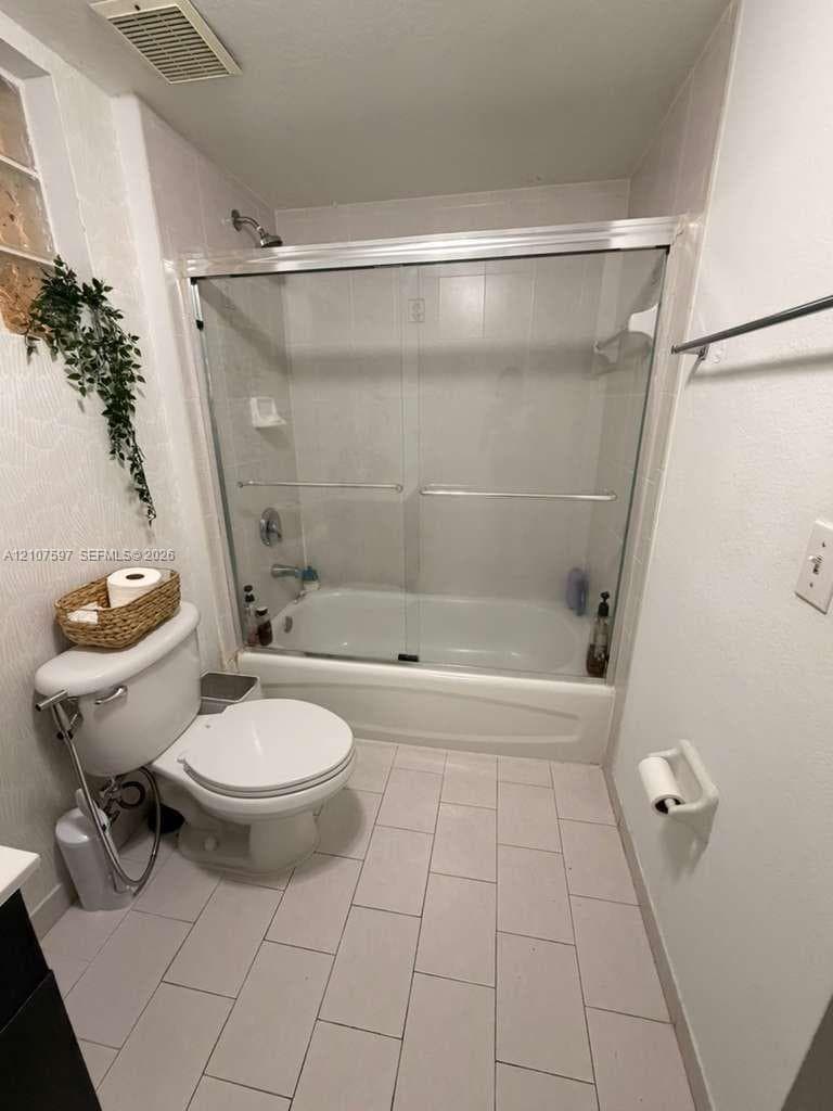 Bathroom featuring a shower and bathtub combination with a glass sliding door, ceramic tile flooring, and wall-mounted metal towel rack
