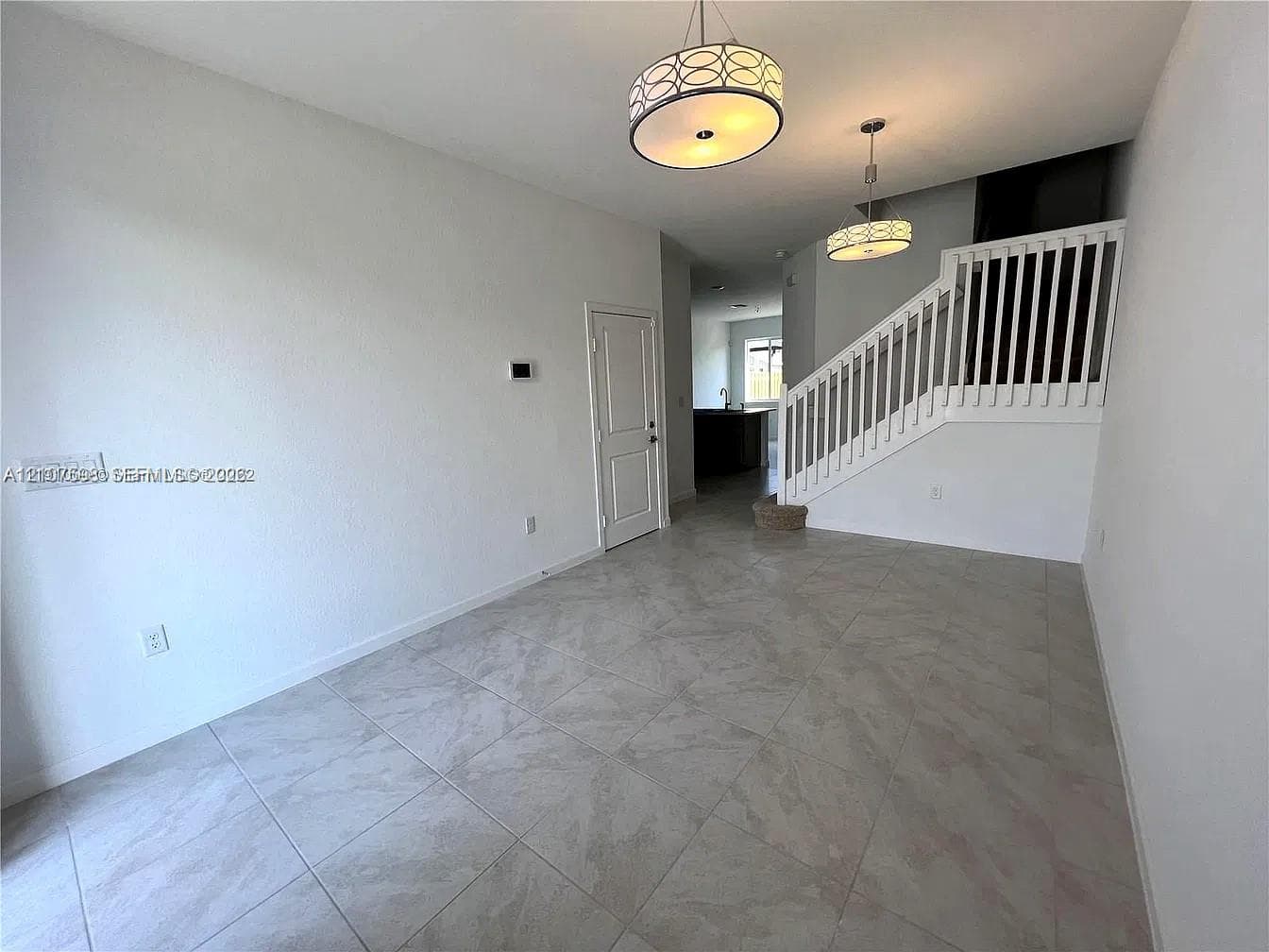 Large-format tile flooring, dual drum pendant lighting, and a staircase featuring a white wooden balustrade