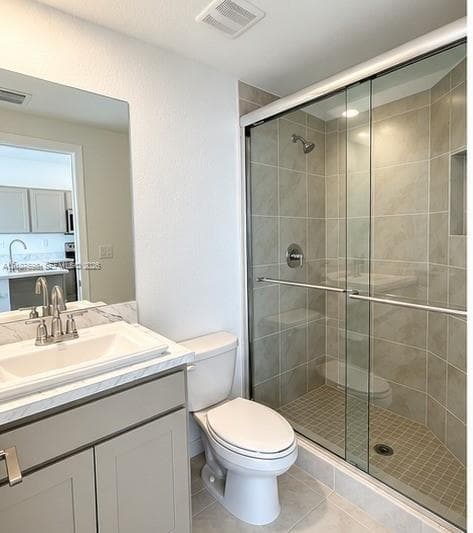 Bathroom featuring a vanity with light-toned cabinetry, solid surface countertop with integrated basin, shower with sliding glass doors and ceramic wall tile, and built-in shower niche