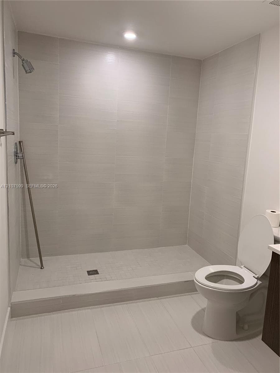 Walk-in shower with floor-to-ceiling textured tile surround, built-in metal shower fixtures, recessed ceiling lighting, and large-format tile flooring