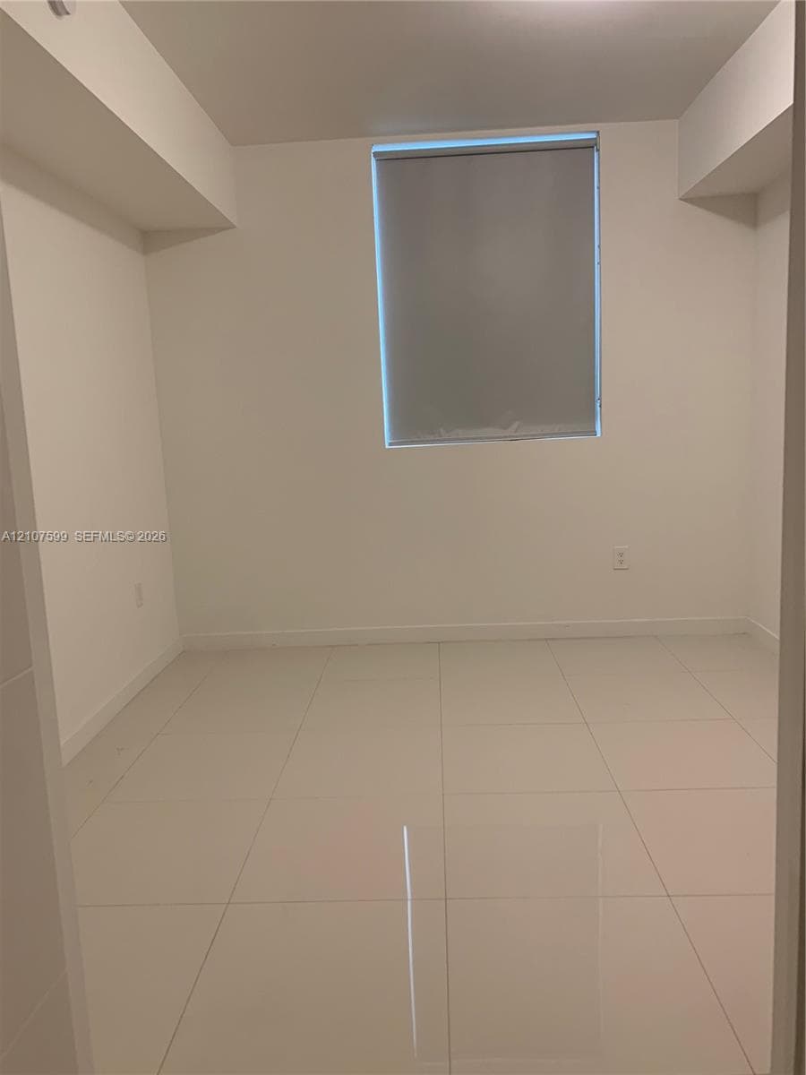 Neutral interior space featuring polished tile flooring, crisp white walls, and a recessed window with a pull-down roller shade