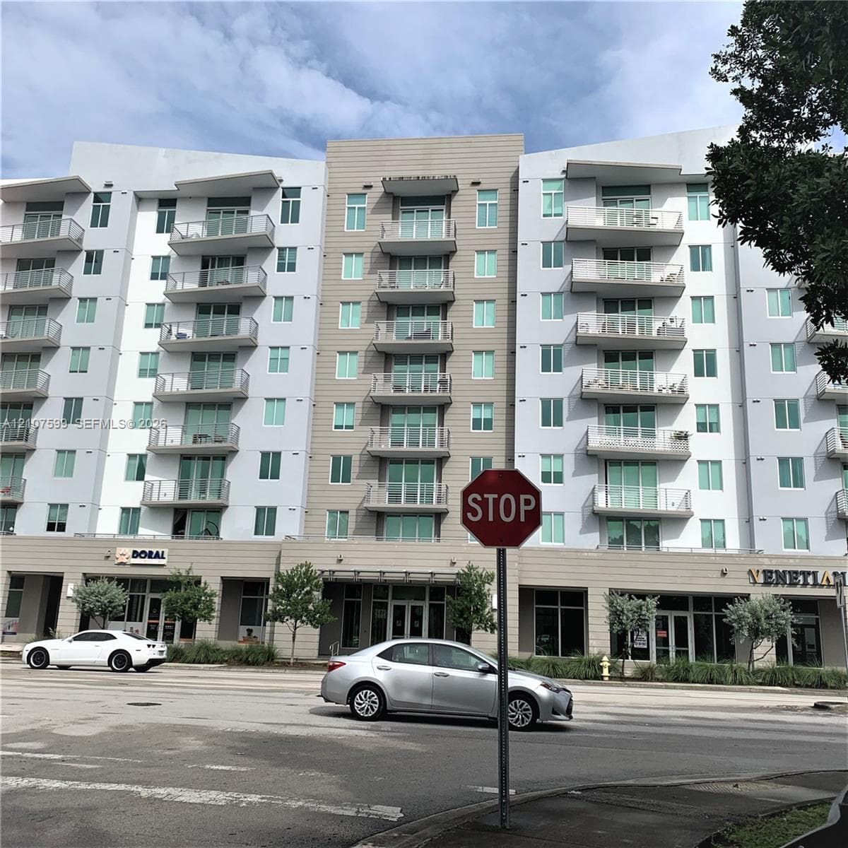 Multi-story building exterior featuring a mixed-material facade, private glass-railed balconies, and ground-level commercial storefronts