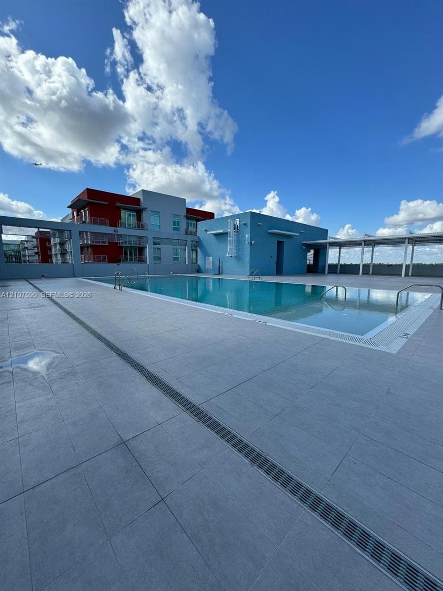Rooftop swimming pool featuring large-format tile decking, metallic safety rails, and a covered patio structure