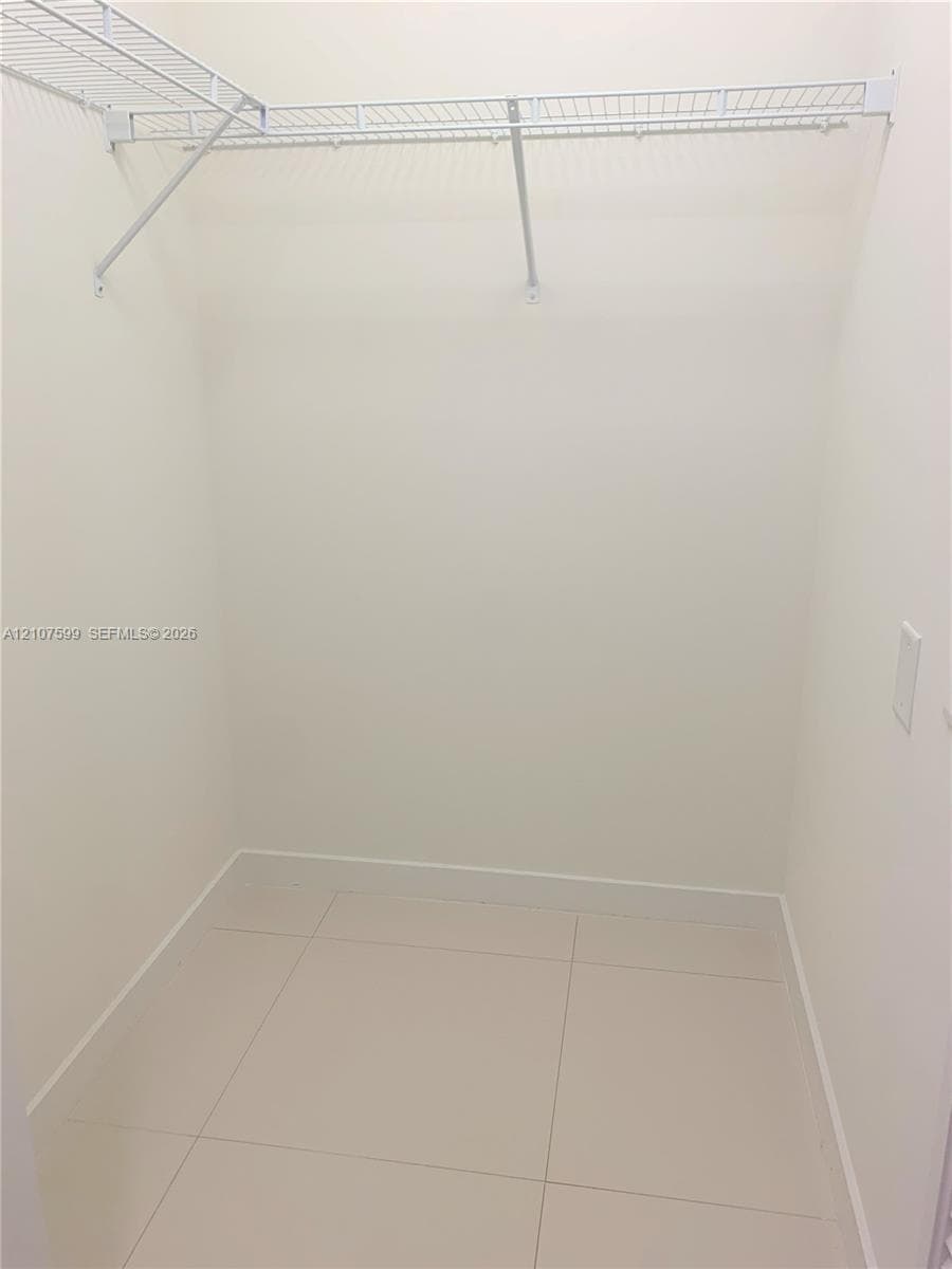 Walk-in storage space featuring large-format neutral floor tile and white coated-wire shelving