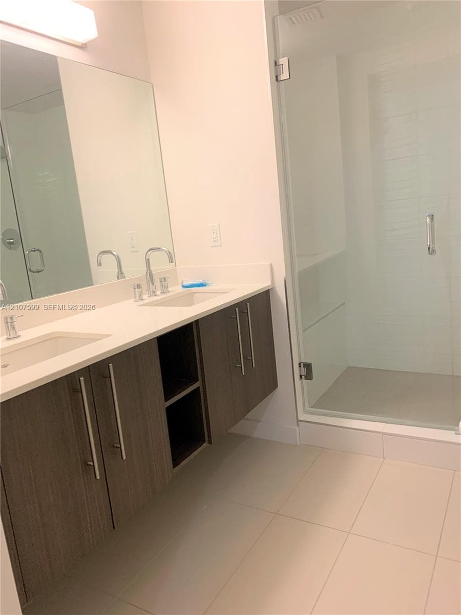 Floating dual-sink vanity with wood-finish cabinetry, solid-surface countertop, and glass-enclosed shower with tiled flooring
