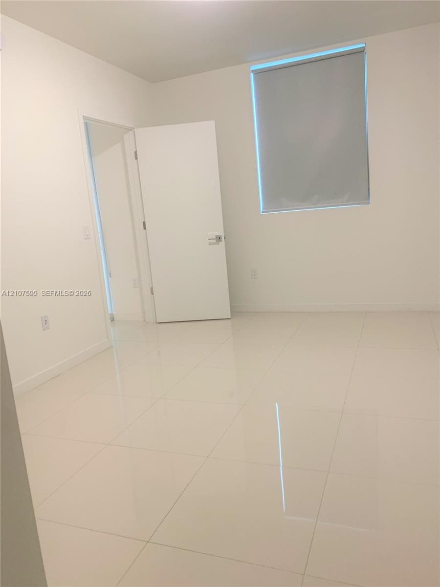 Interior space featuring high-gloss tile flooring, smooth neutral walls, and a single-panel interior door with brushed metal hardware