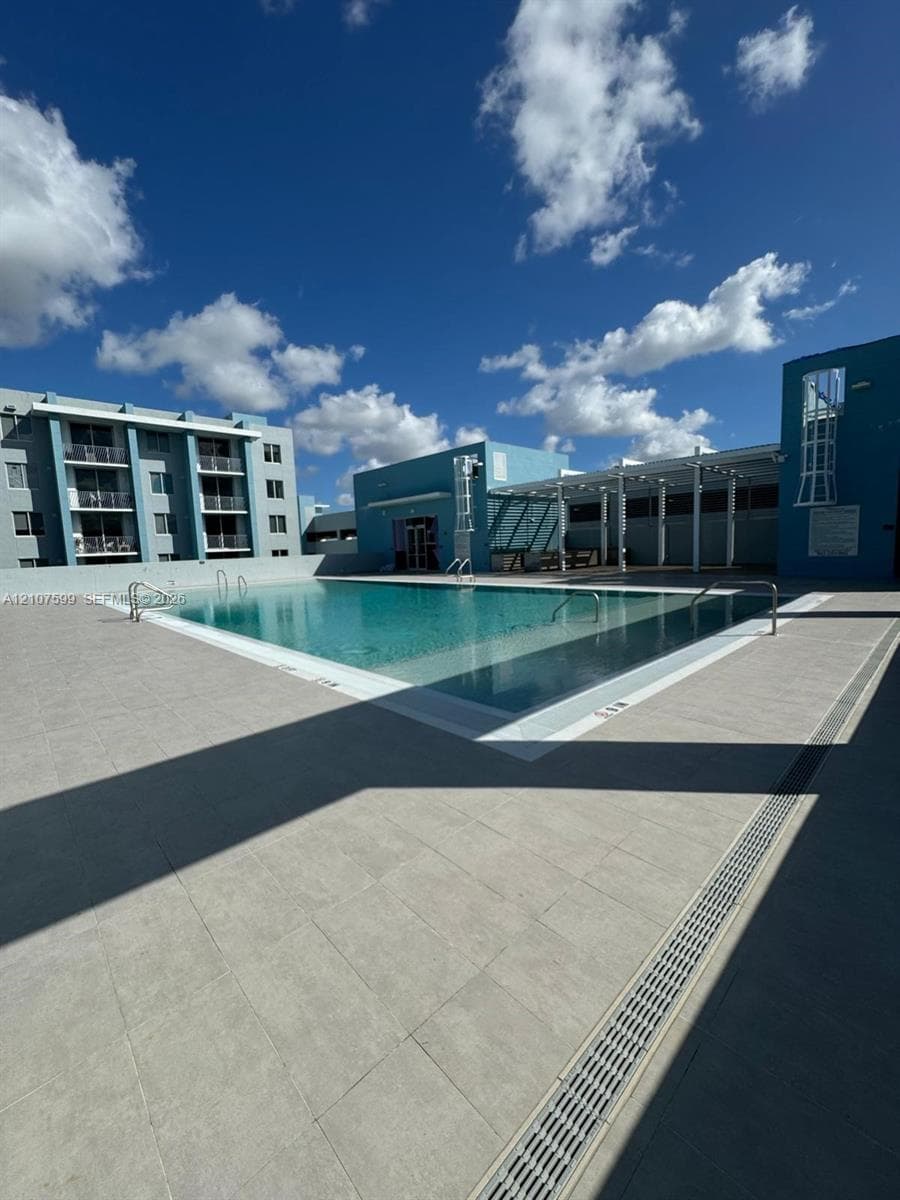 Swimming pool with tile surround, metal pool ladders, pergola-covered deck area, and multi-story building exterior