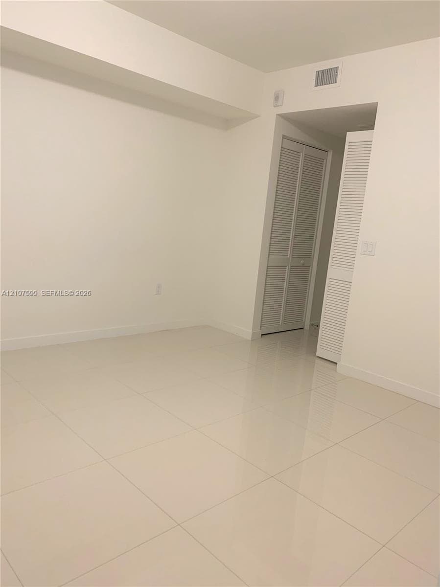Interior space featuring large-format tile flooring, neutral walls, and dual louvered-style closet doors