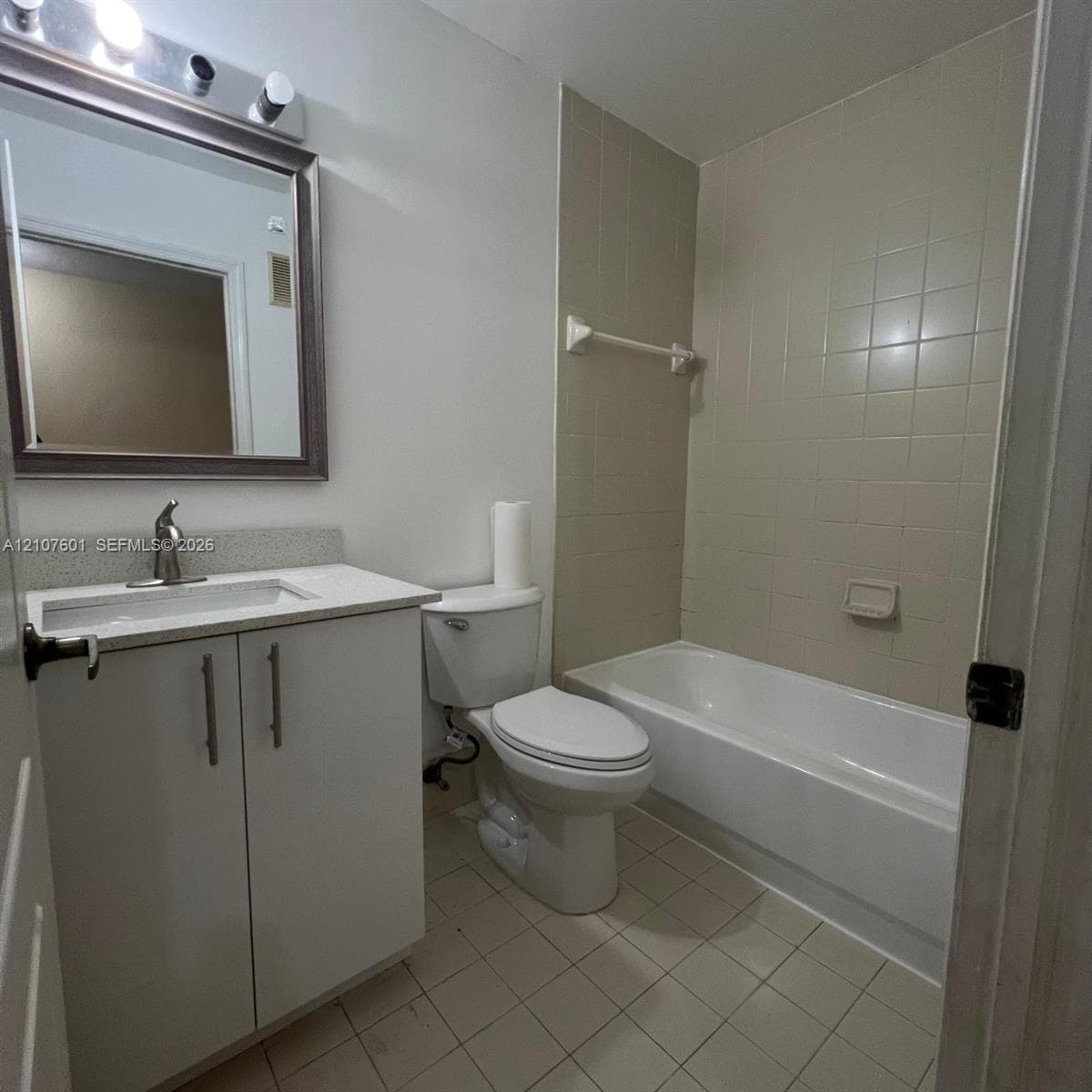 Bathroom featuring a white vanity cabinet with a stone-composite countertop, undermount sink, ceramic-tile tub surround, and three-bulb vanity lighting