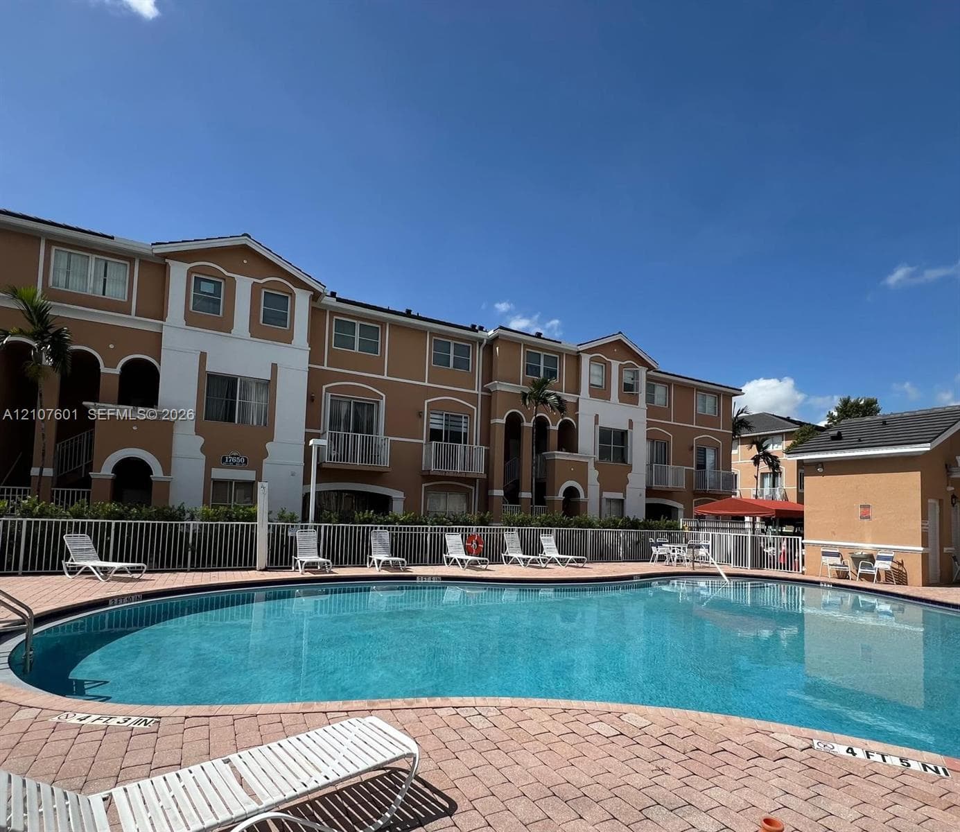 Community pool featuring a curved design, brick-paver decking, and metal fencing