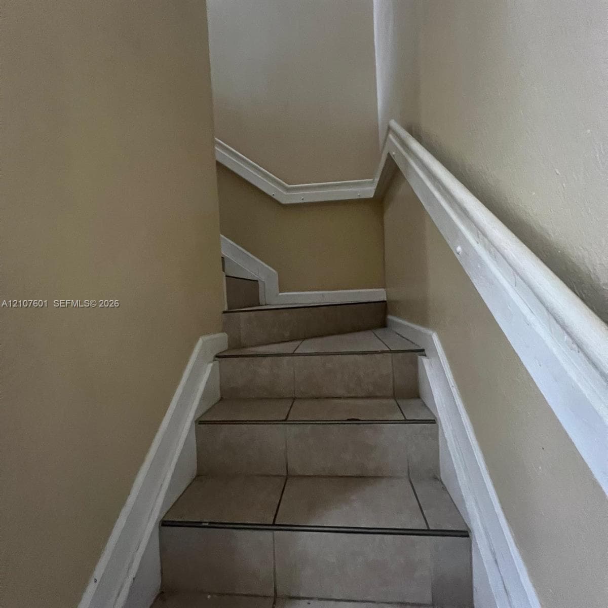 Staircase featuring large-format neutral tile treads, white painted millwork, and a sturdy white handrail