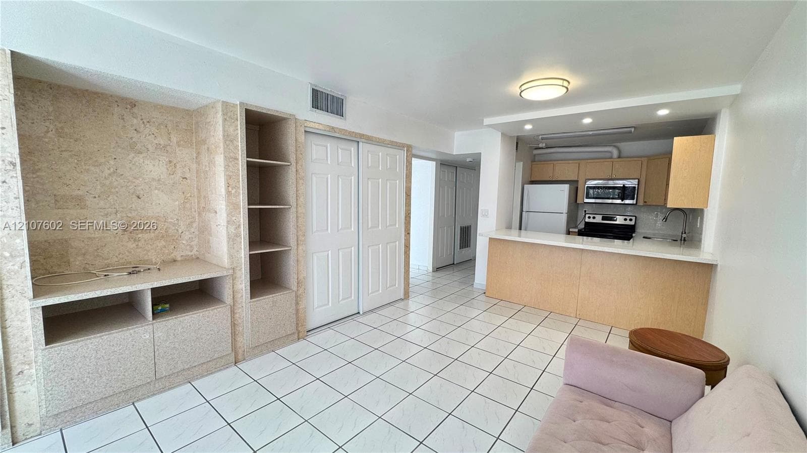 Open-concept kitchen featuring a breakfast bar, stone-tile-finished built-in cabinetry, ceramic tile flooring, and integrated stainless steel appliances