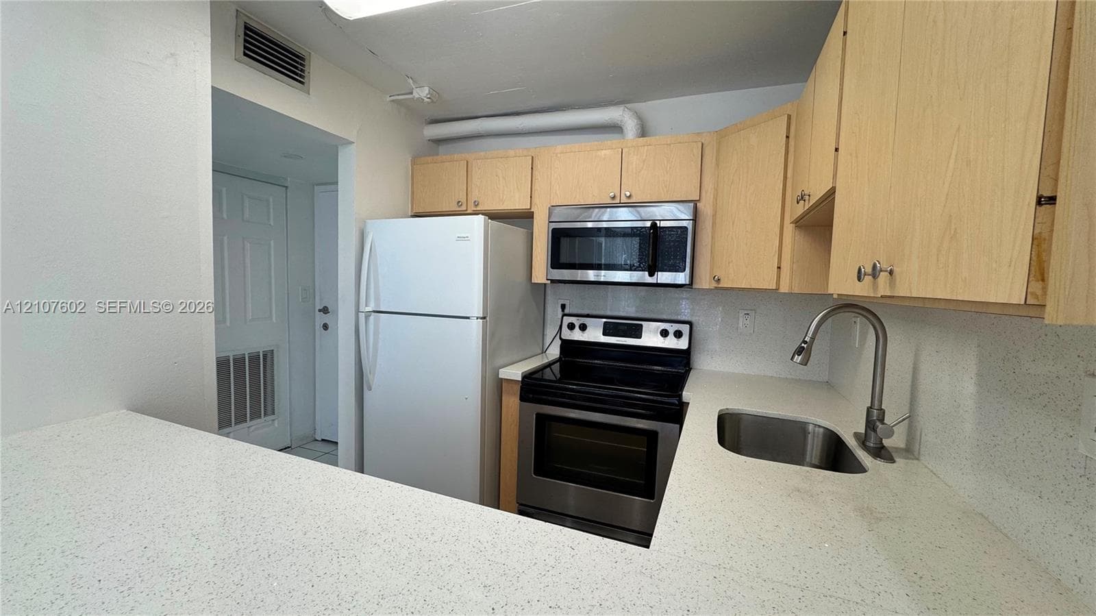Kitchen featuring light-finish cabinetry, solid surface countertops, stainless steel appliances, and a stainless steel gooseneck faucet
