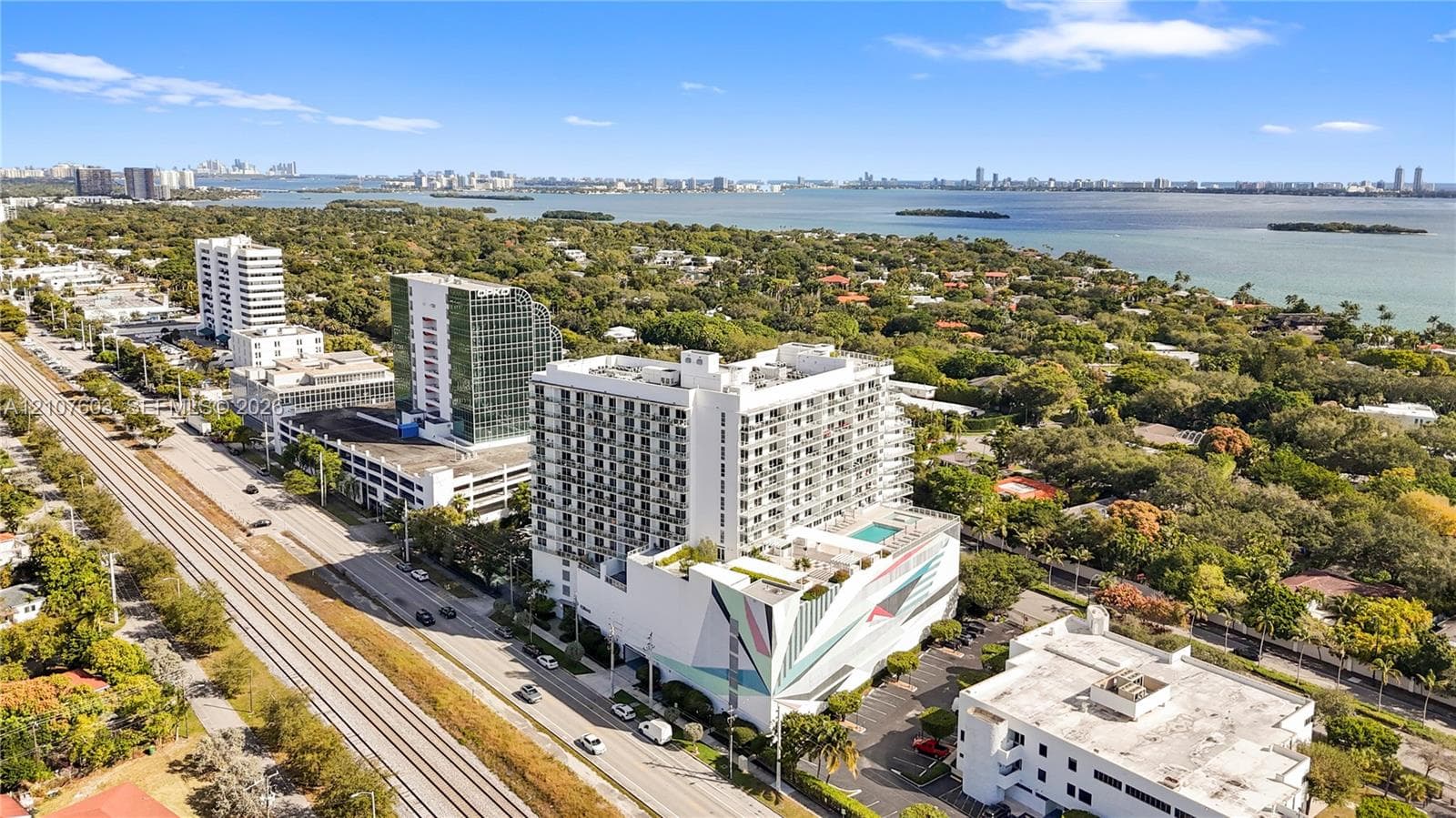 Aerial perspective featuring a mid-rise residential structure with a rooftop swimming pool and a prominent exterior geometric mural, located in a coastal setting