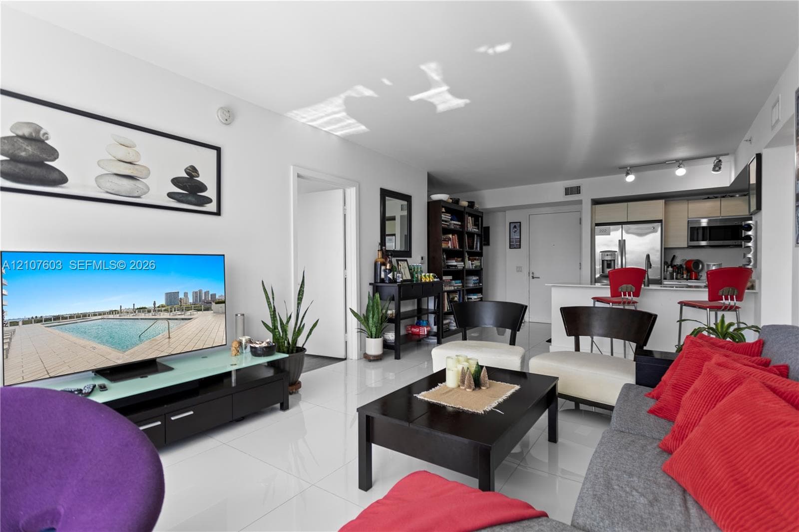 Open-concept living space featuring high-gloss tile flooring, recessed track lighting, and a kitchen peninsula with a white stone-finish countertop
