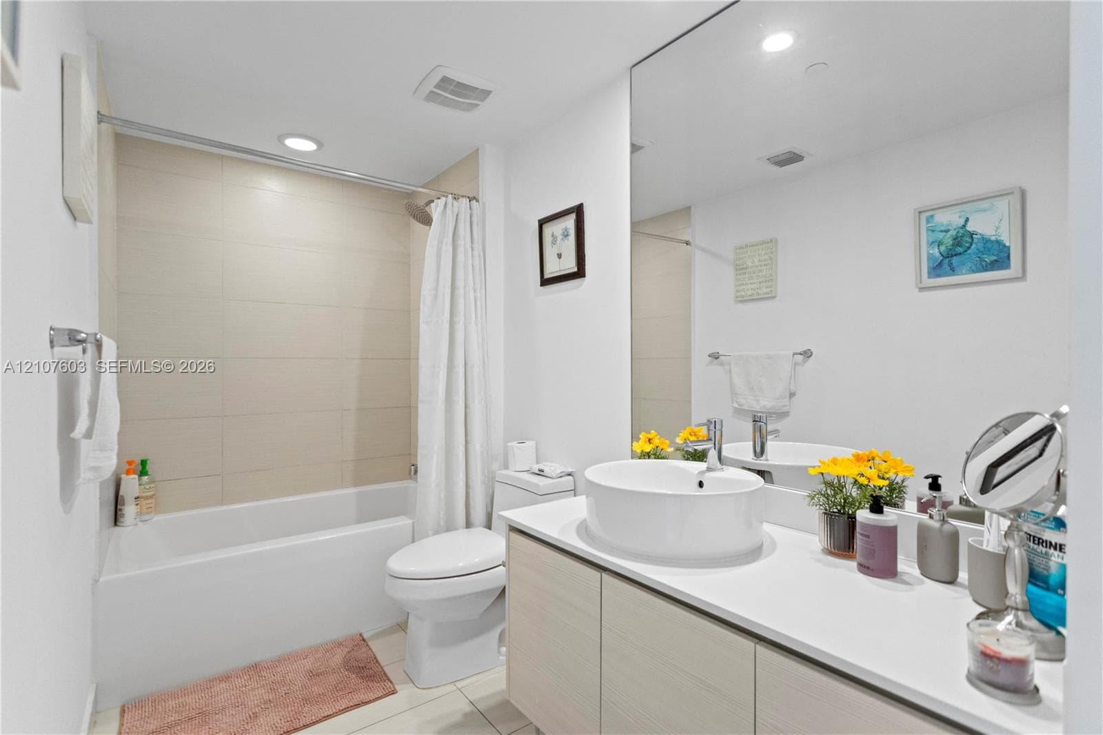 Bathroom featuring a vessel sink, quartz-finish countertop, light-toned cabinetry, floor-to-ceiling wall mirror, and a tub with a tile-surround wall