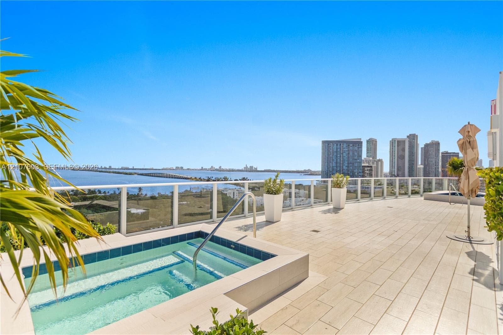 Expansive outdoor terrace featuring light-toned tile flooring, an in-ground spa with tile surround, and a glass-paneled railing