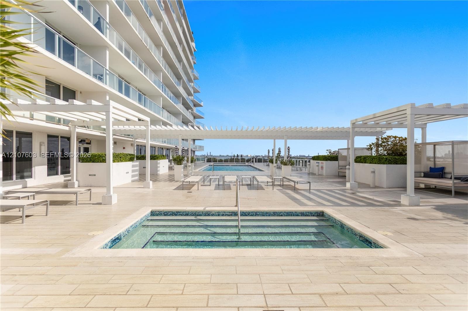 Outdoor terrace featuring a tiled deck, built-in swimming pool with step entry, mosaic tile accents, white pergola structures, and integrated concrete planters