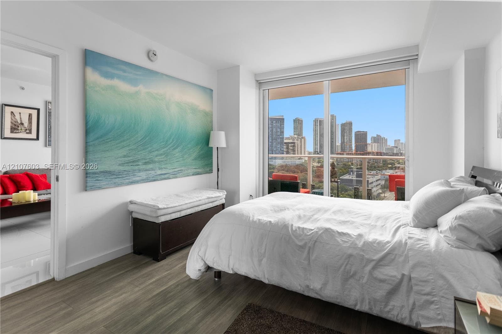 Floor-to-ceiling windows featuring a cityscape backdrop, private balcony with metal railing, and wood-finish flooring