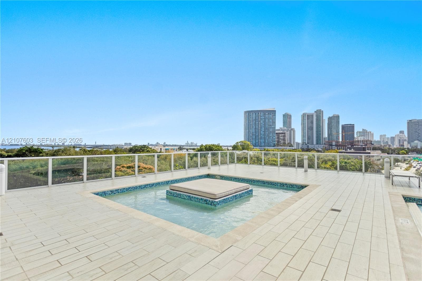 Rooftop terrace featuring large-format tile flooring, a central built-in water feature with mosaic tile accents, a glass panel railing system, and an expansive cityscape backdrop