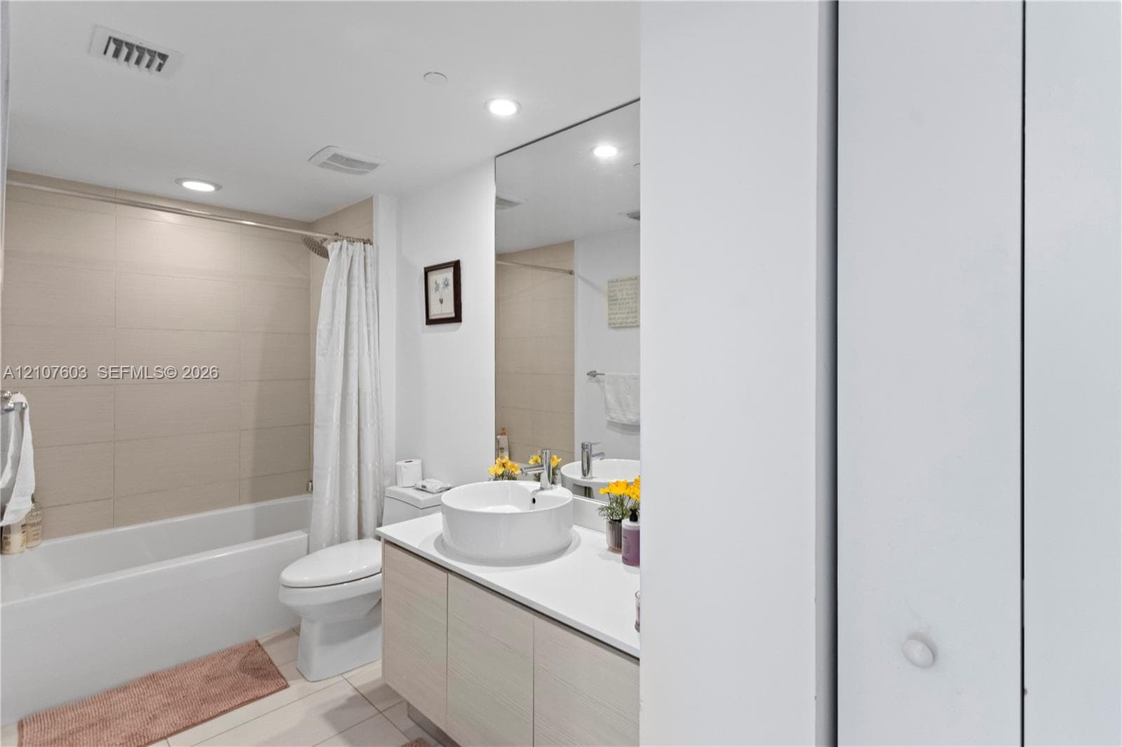 Bathroom featuring a vanity with wood-finish cabinetry, a white countertop, a circular vessel sink, wall-spanning mirror, and a tub-shower combination with large-format wall tile