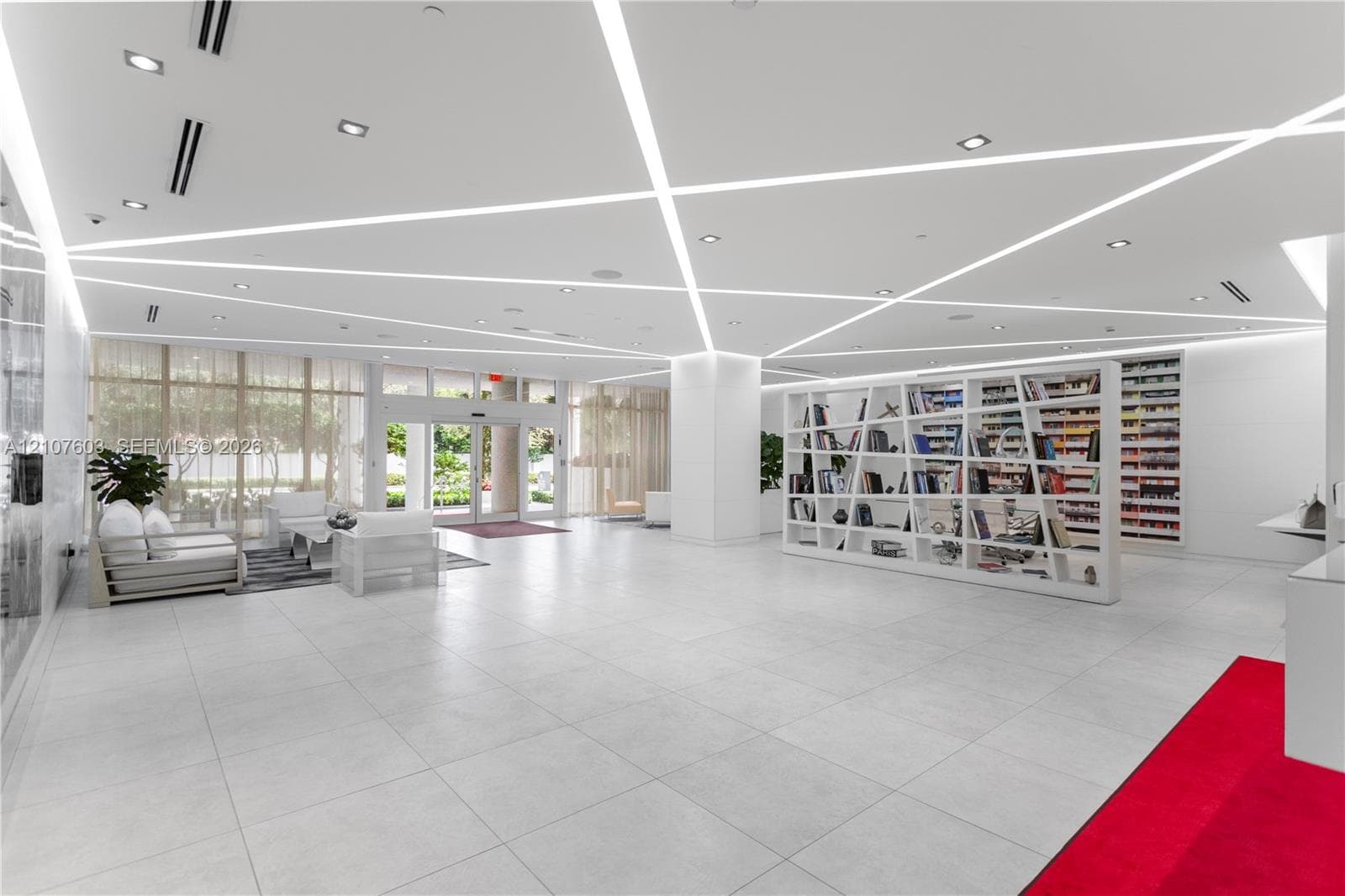 Large-format tile flooring, geometric ceiling with recessed linear lighting, full-height glass entrance doors, and built-in architectural shelving