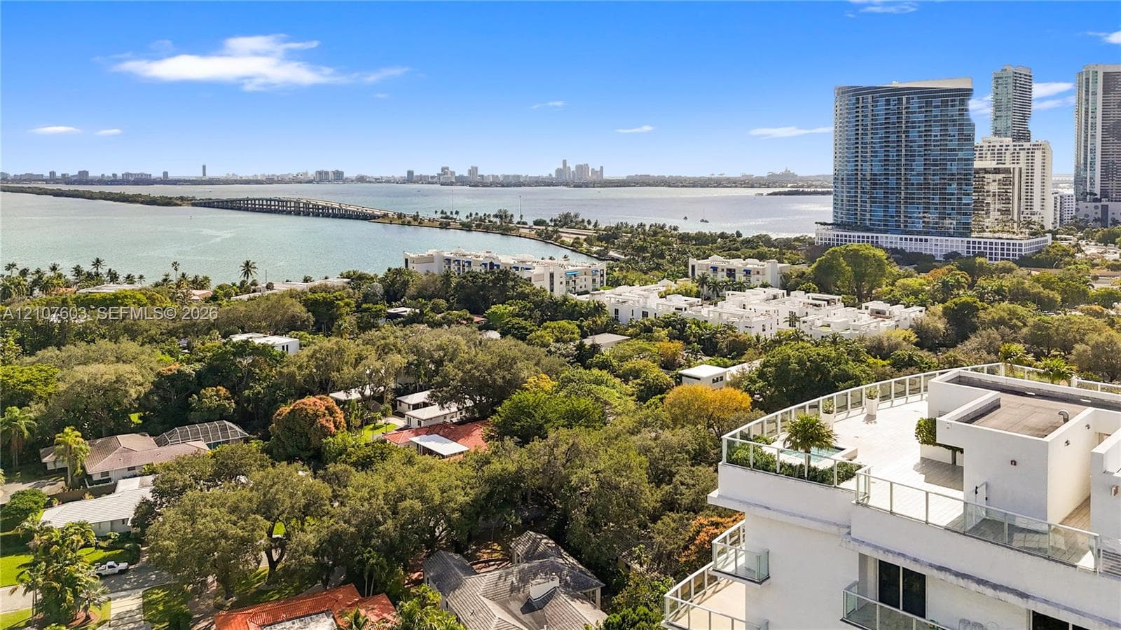 Aerial perspective featuring a multi-story residential building with a glass-railed rooftop terrace, integrated hardscaping, and surrounding mature tree canopy