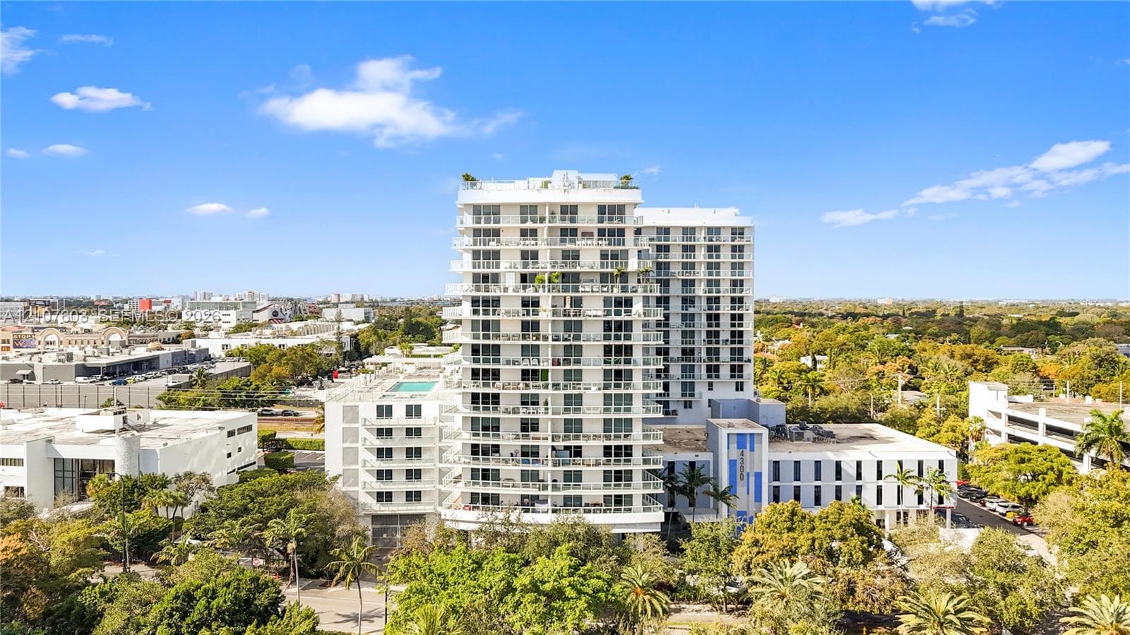 High-rise residential building featuring private recessed balconies, a rooftop pool, glass railing systems, and extensive manicured landscaping