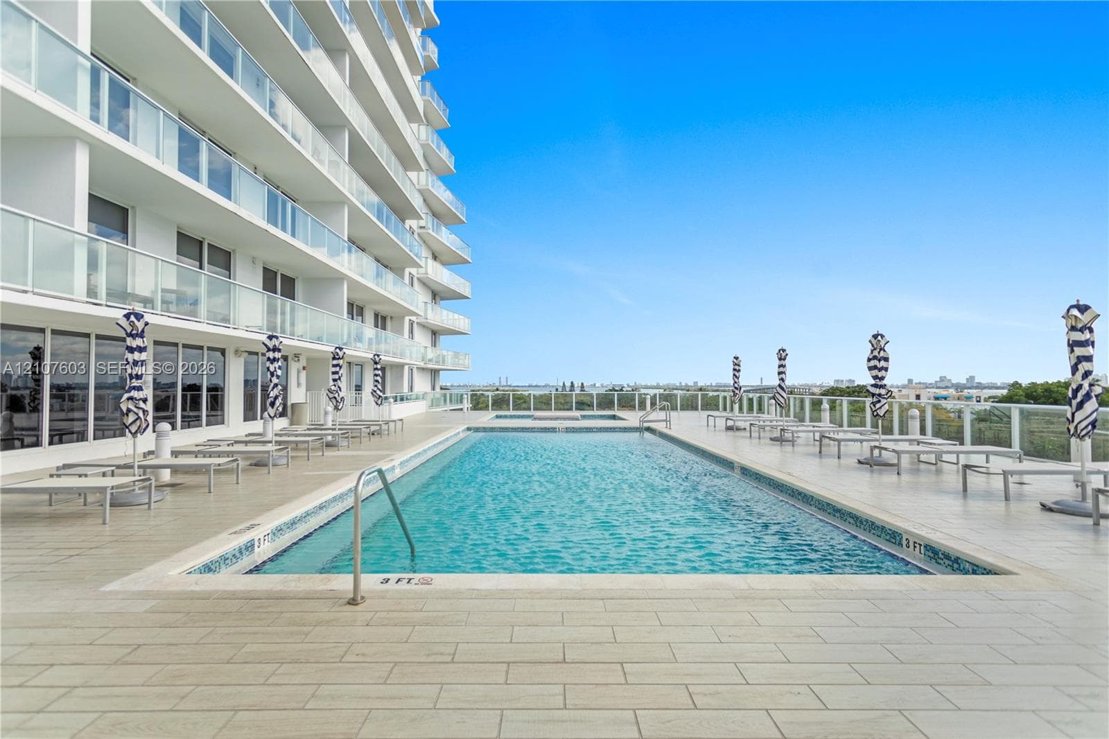 Rectangular swimming pool featuring a tile surround, metal handrail, perimeter glass panel fencing, and wood-finish tile decking