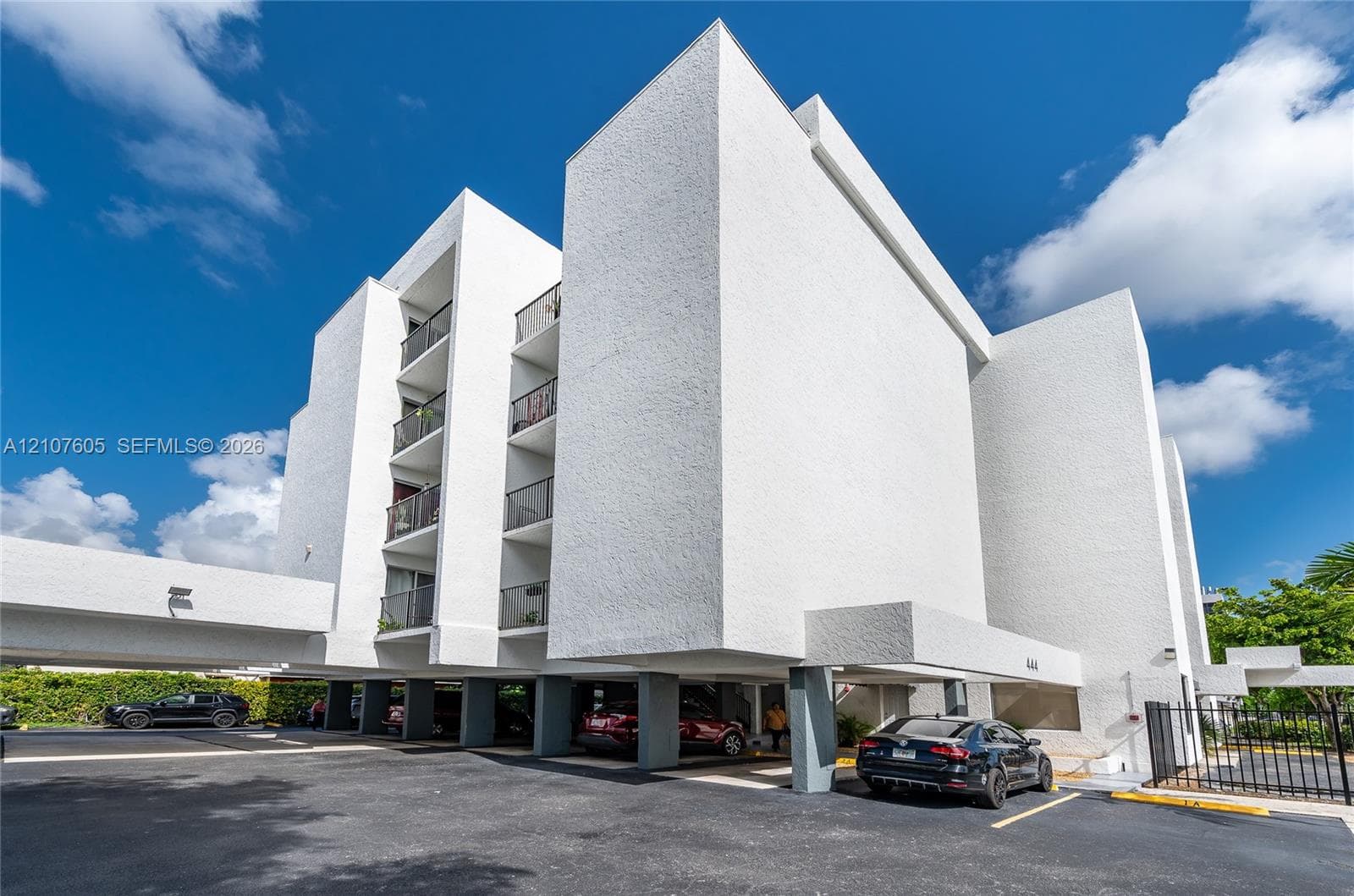 Multi-story architectural exterior featuring a textured white finish, covered ground-level parking, and stacked balconies