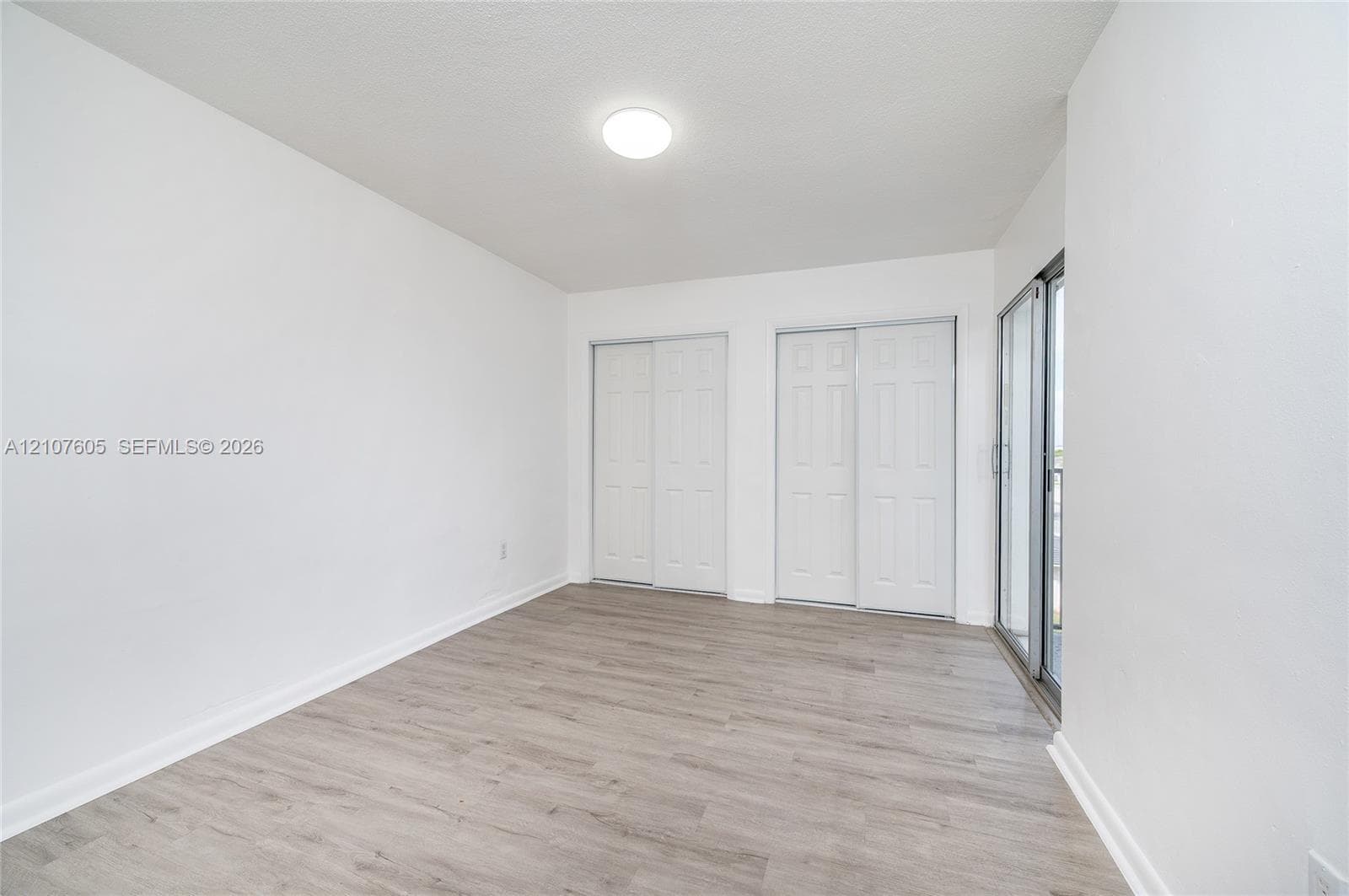 Room featuring wood-finish flooring, two sets of white double-door closets, and a glass sliding door