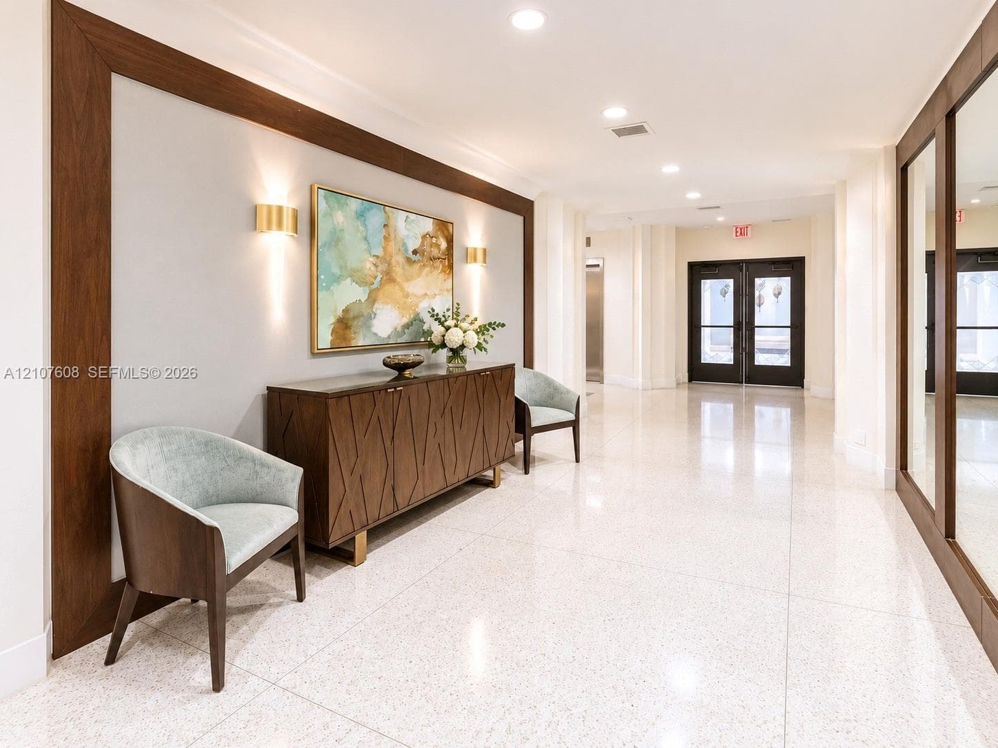 Polished stone flooring, wood-framed wall detailing, recessed ceiling lighting, and brass-finish wall-mounted sconces