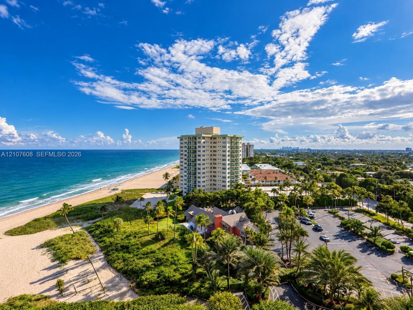 Aerial perspective featuring direct oceanfront access, sandy shoreline, mature tropical landscaping, and paved parking area