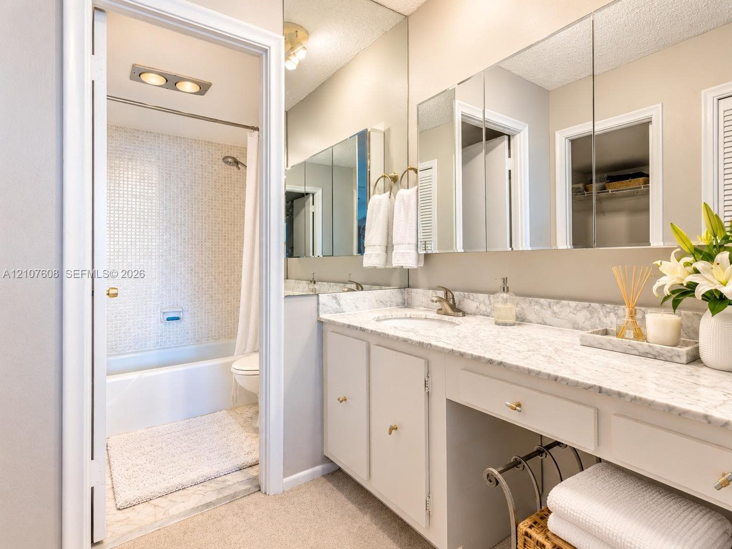 Bathroom featuring a stone-top vanity with an integrated sink, full-width mirrored medicine cabinet, and a tiled shower-tub combination