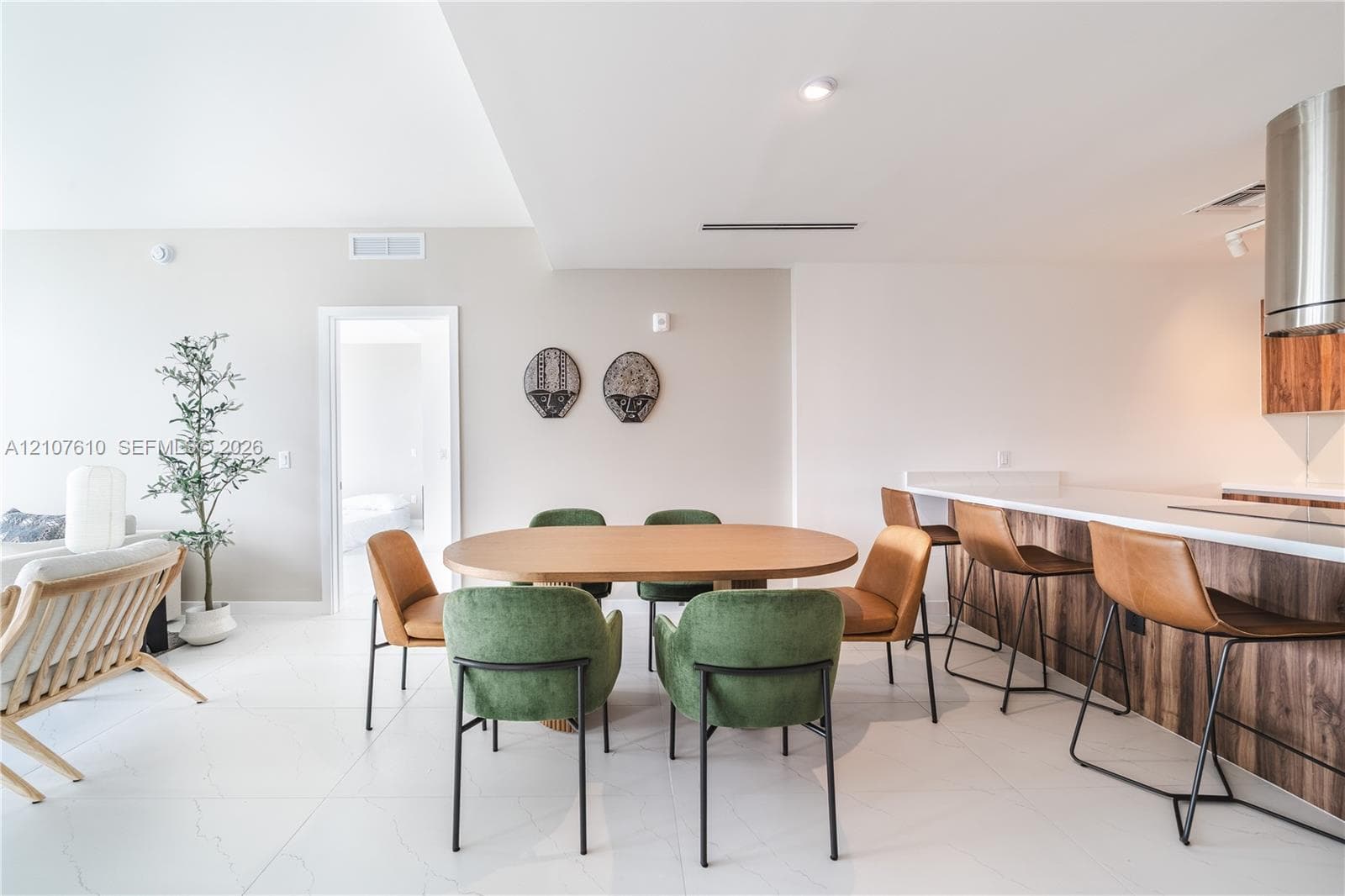 Open-concept kitchen featuring a breakfast bar with wood-finish cabinetry, white solid-surface countertops, and a stainless steel cylinder range hood