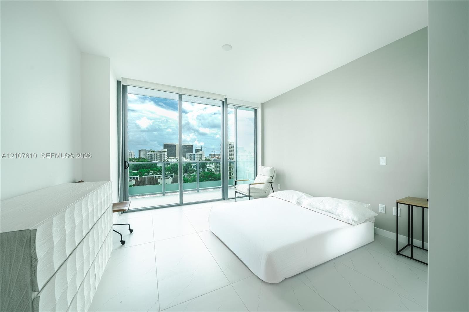 Floor-to-ceiling sliding glass doors, private balcony, neutral large-format tile flooring, and light-filled minimalist interior