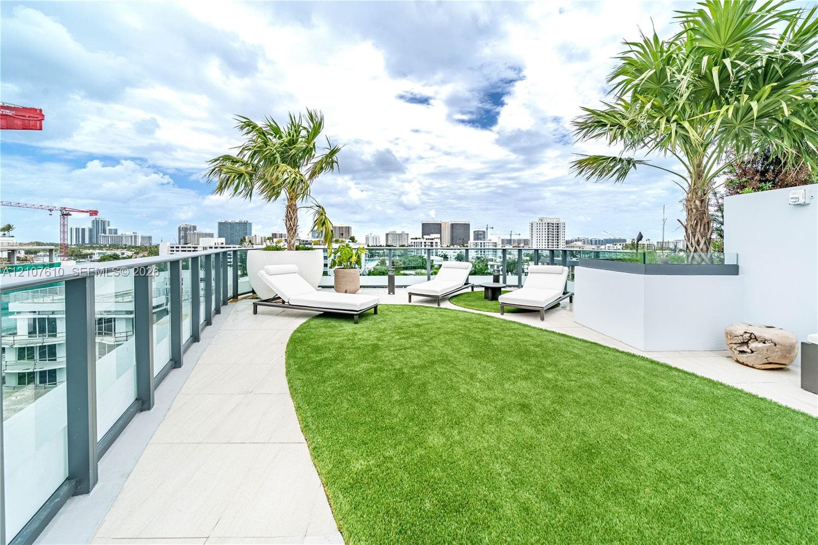 Rooftop terrace featuring large-format tile flooring, artificial turf lawn, glass panel perimeter railing, and built-in masonry planters
