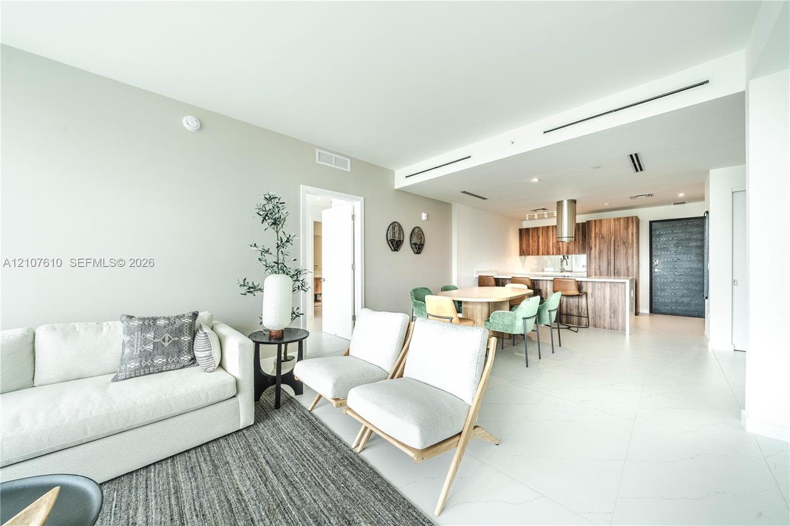 Open-concept interior featuring large-format tile flooring, recessed ceiling lighting, and a kitchen equipped with wood-finish cabinetry, a waterfall-edge island, and a stainless steel cylinder range hood