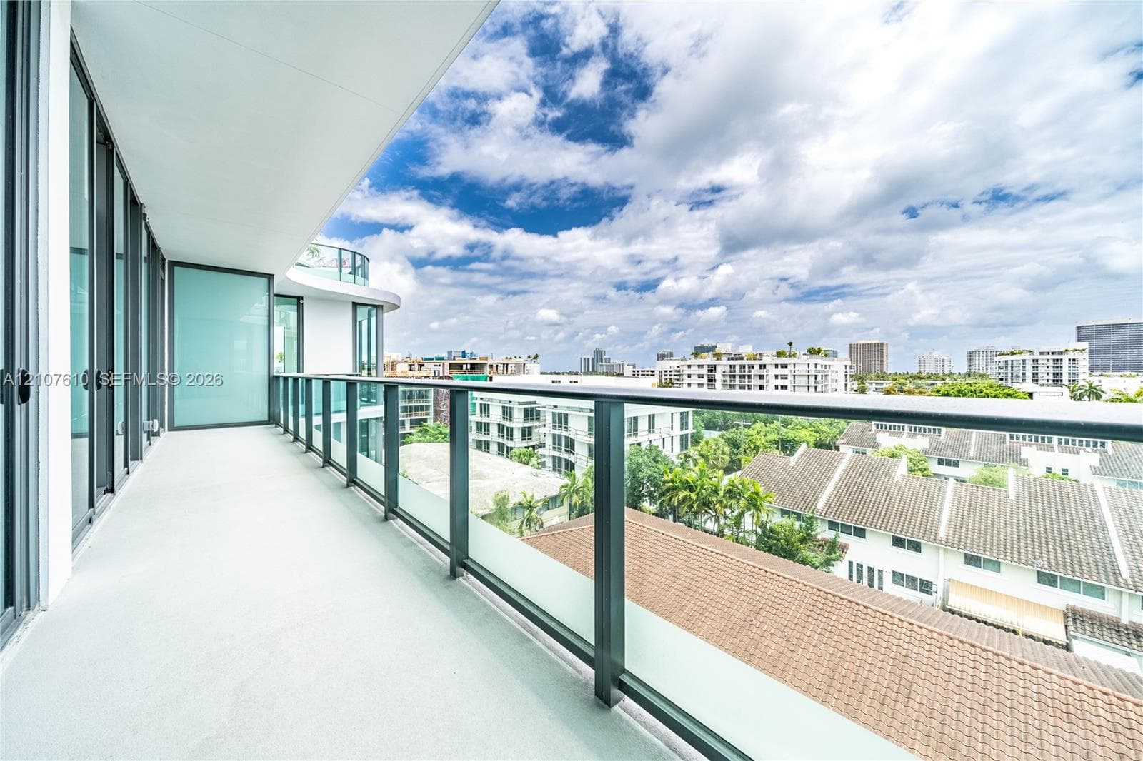Covered balcony featuring a sleek glass-panel railing, concrete-finish flooring, and expansive floor-to-ceiling glass wall panels