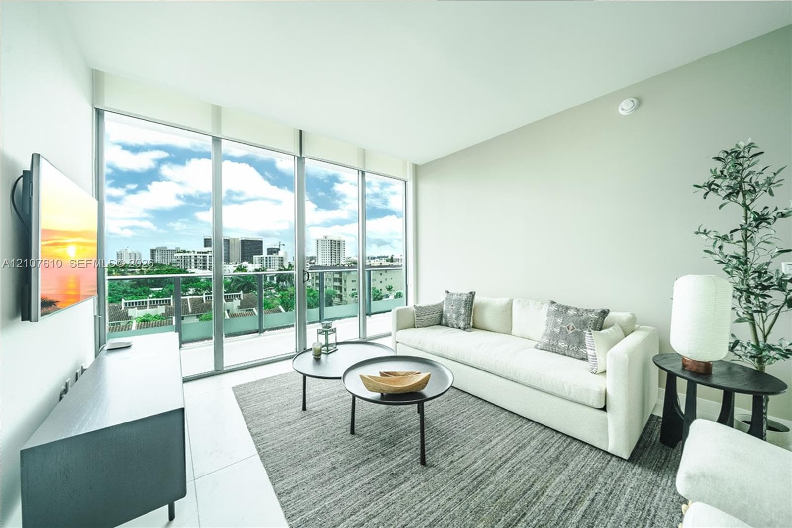 Floor-to-ceiling windows, glass-panel balcony railing, neutral tile flooring, and urban landscape backdrop