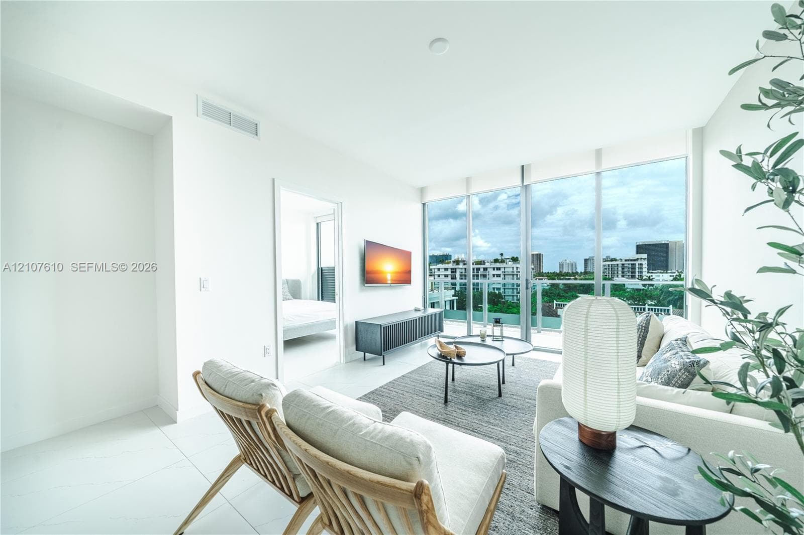 Living area featuring floor-to-ceiling windows, natural tile flooring, and a glass-paneled balcony