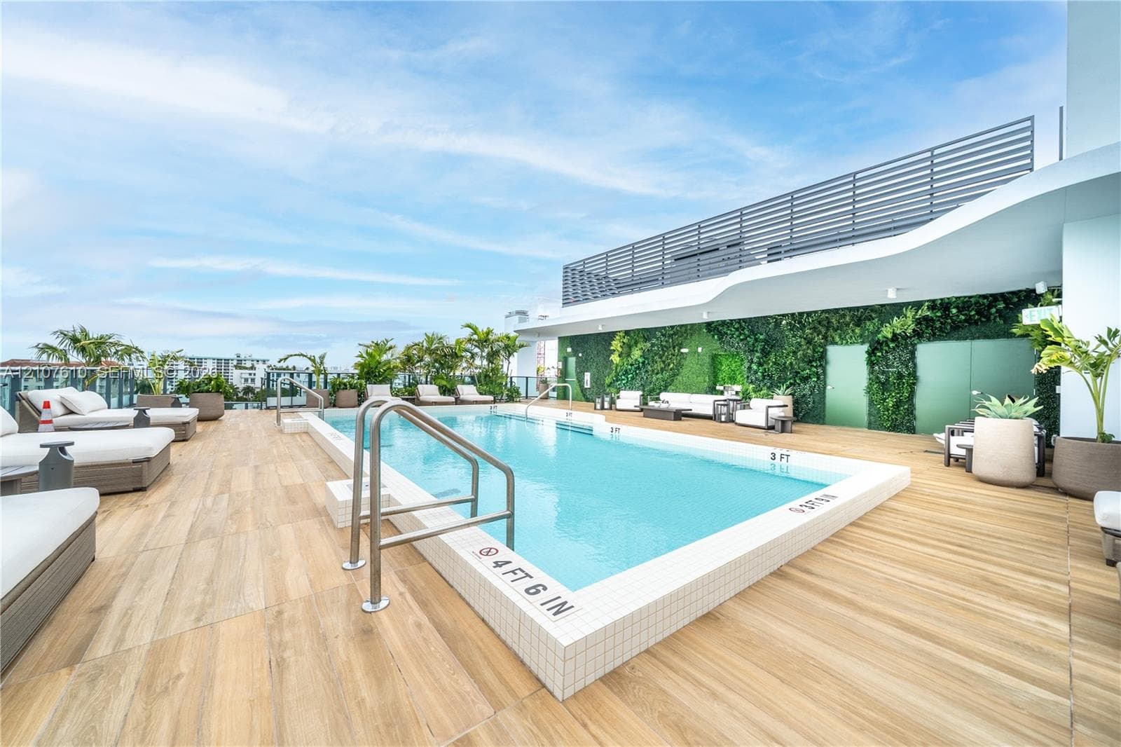 Rooftop swimming pool with metallic handrails, wood-finish tile decking, and a vertical garden wall