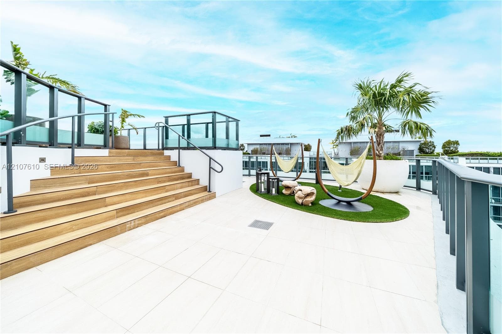 Rooftop terrace featuring large-format tile flooring, wood-finish stair treads, glass panel railings with metal handrails, and a designated artificial turf area
