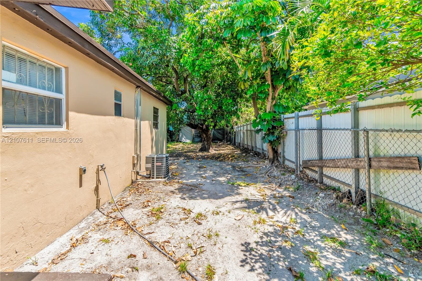 Side exterior featuring a stucco facade, horizontal slider windows, and a chain-link fence perimeter