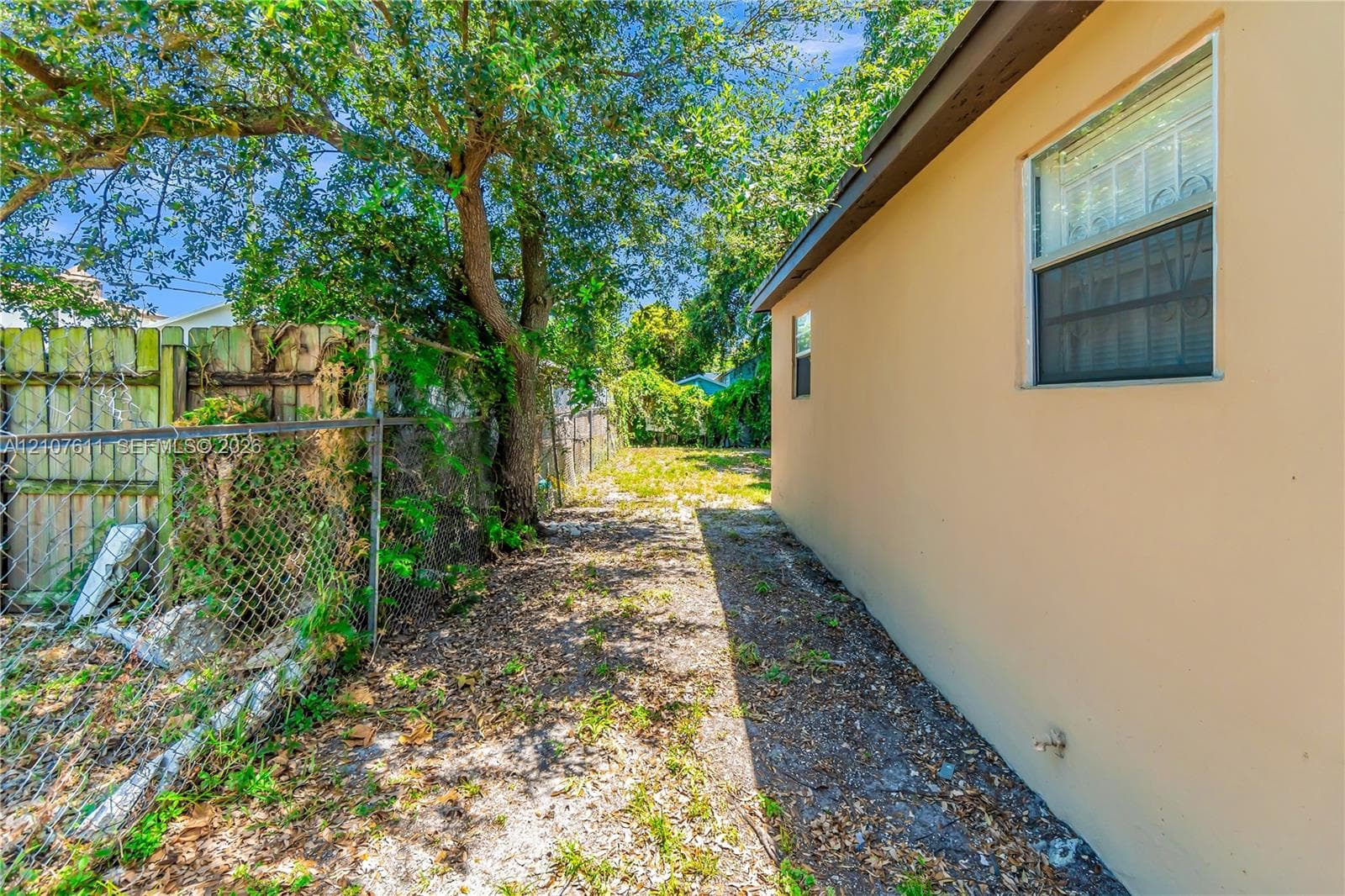Exterior side yard featuring stucco siding, single-hung windows, and chain-link perimeter fencing