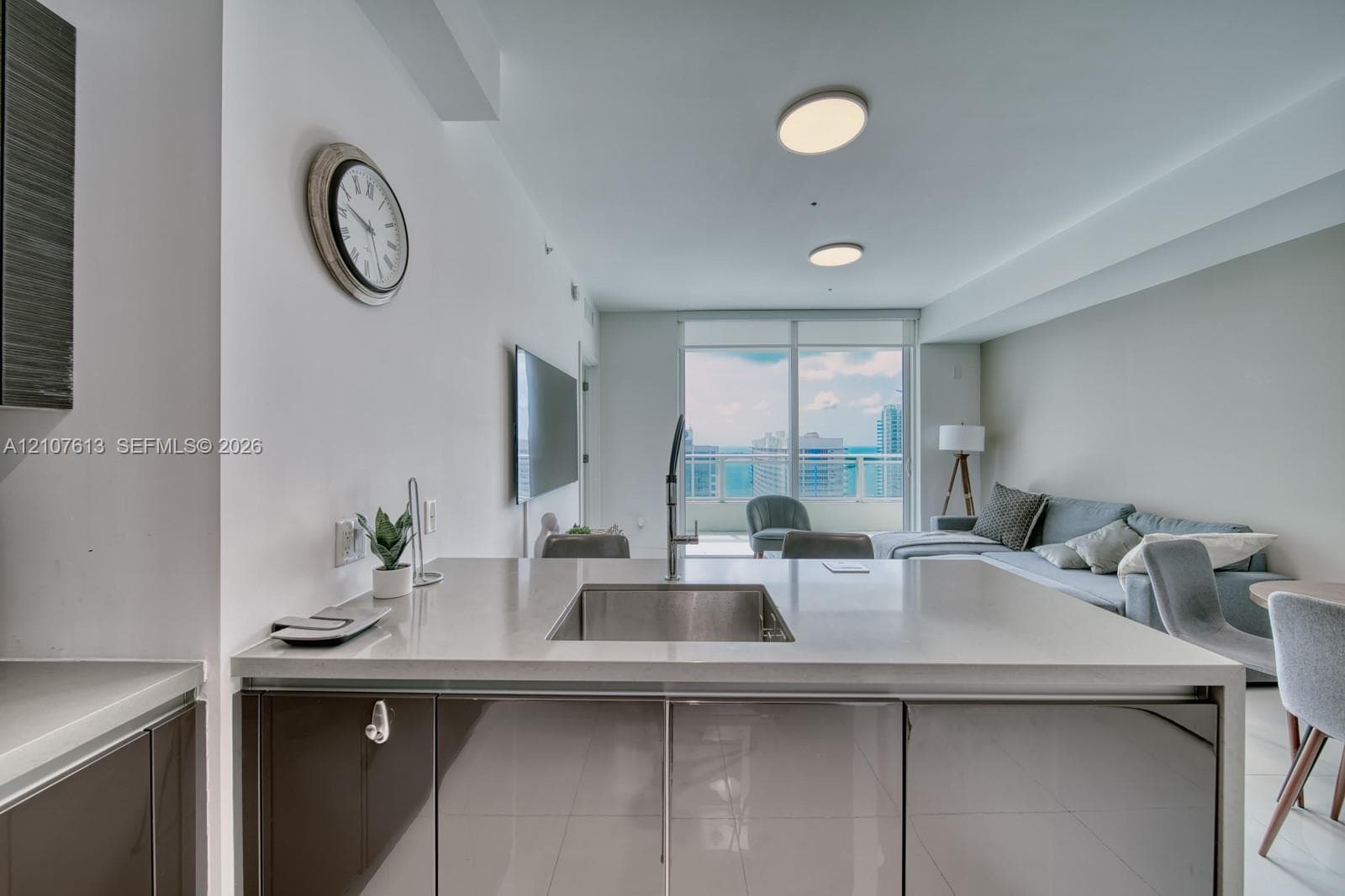 Kitchen island featuring a solid-surface countertop, under-mount stainless steel sink, gooseneck faucet, and high-gloss cabinetry, illuminated by recessed ceiling lighting