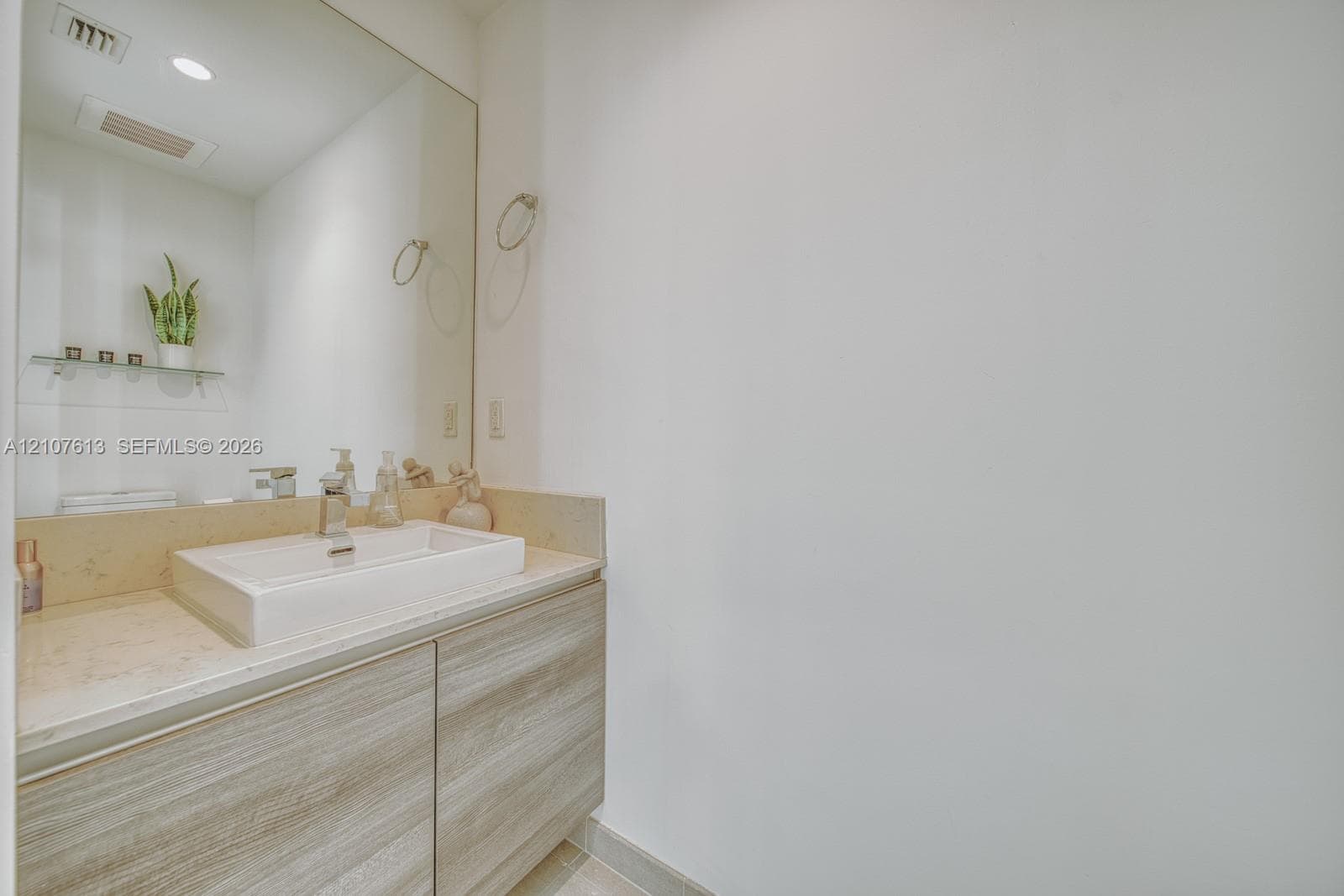 Floating vanity with a light wood-finish cabinet, rectangular vessel sink, solid-surface countertop, and an expansive wall-mounted mirror