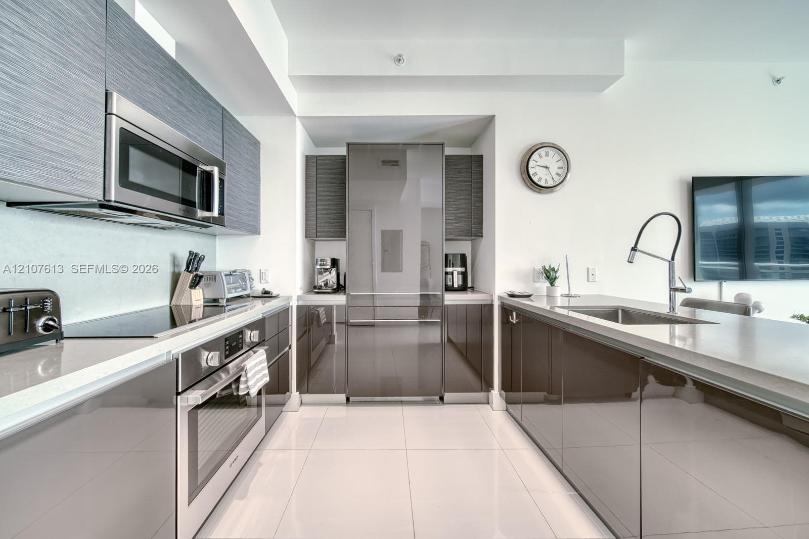 Modern kitchen featuring high-gloss cabinetry, stainless steel appliances, integrated refrigerator, stone-surfaced countertops, and a stainless steel gooseneck faucet