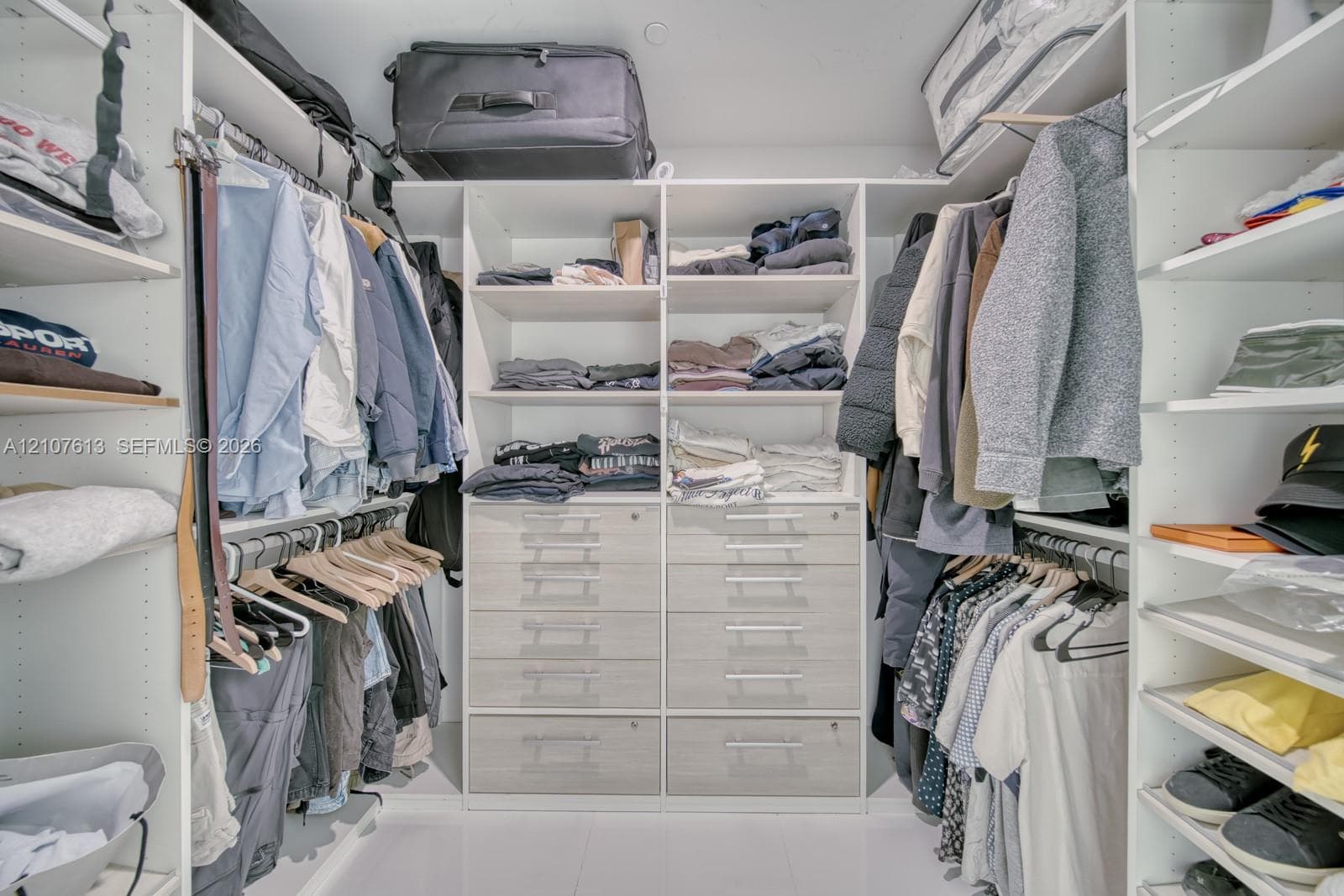 Custom walk-in closet featuring white floor-to-ceiling shelving, integrated wooden-finish cabinetry, built-in organizers, and hanging rods