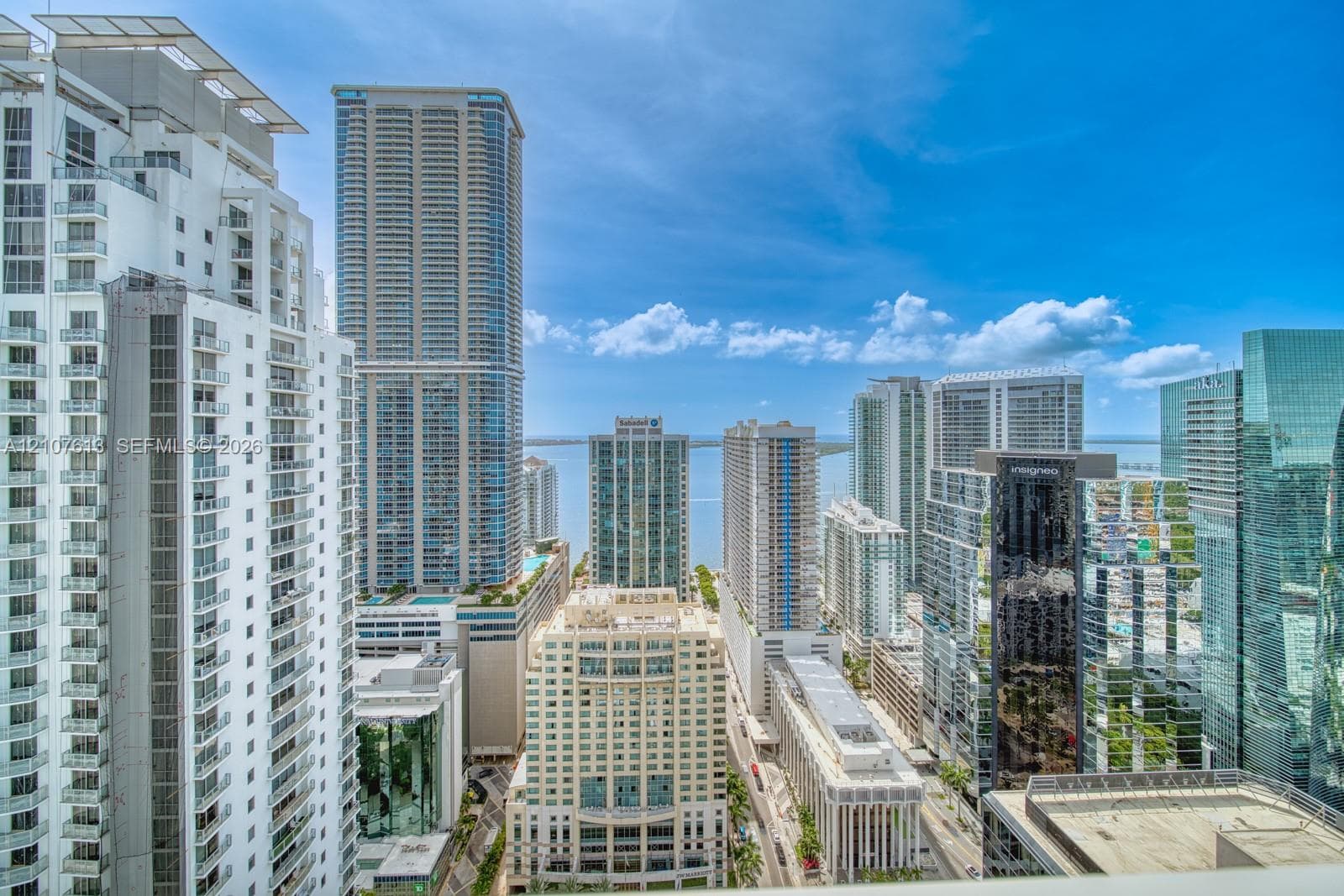High-rise urban landscape featuring multiple glass-facade skyscrapers, balcony-lined residential towers, and a prominent water backdrop